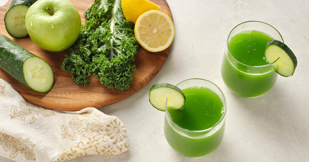 two glasses of green juice surrounded by ingredients