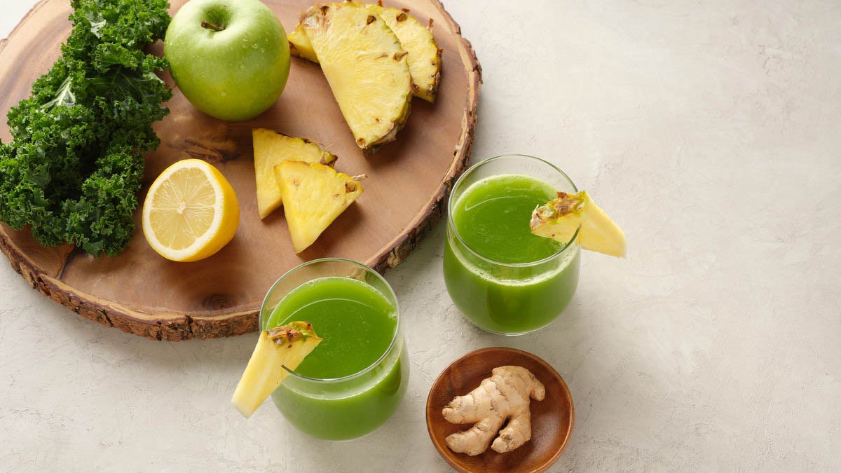 two glasses of cold pressed green juice surrounded by ingredients to make green juice recipe
