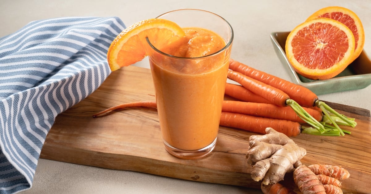 carrot smoothie in a tall glass on a wooden cutting board