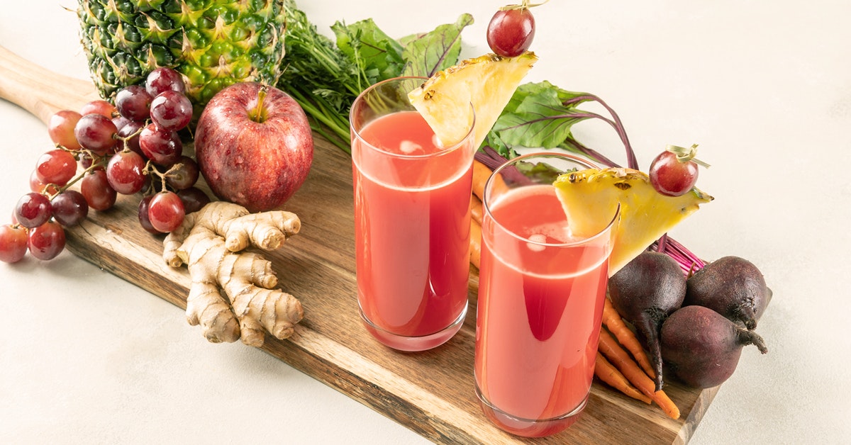 two glasses of red jungle juice surrounded by ingredients on a wooden cutting board