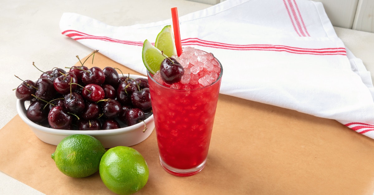 glass of cold pressed sonic cherry limeade on a table with cherries and limes