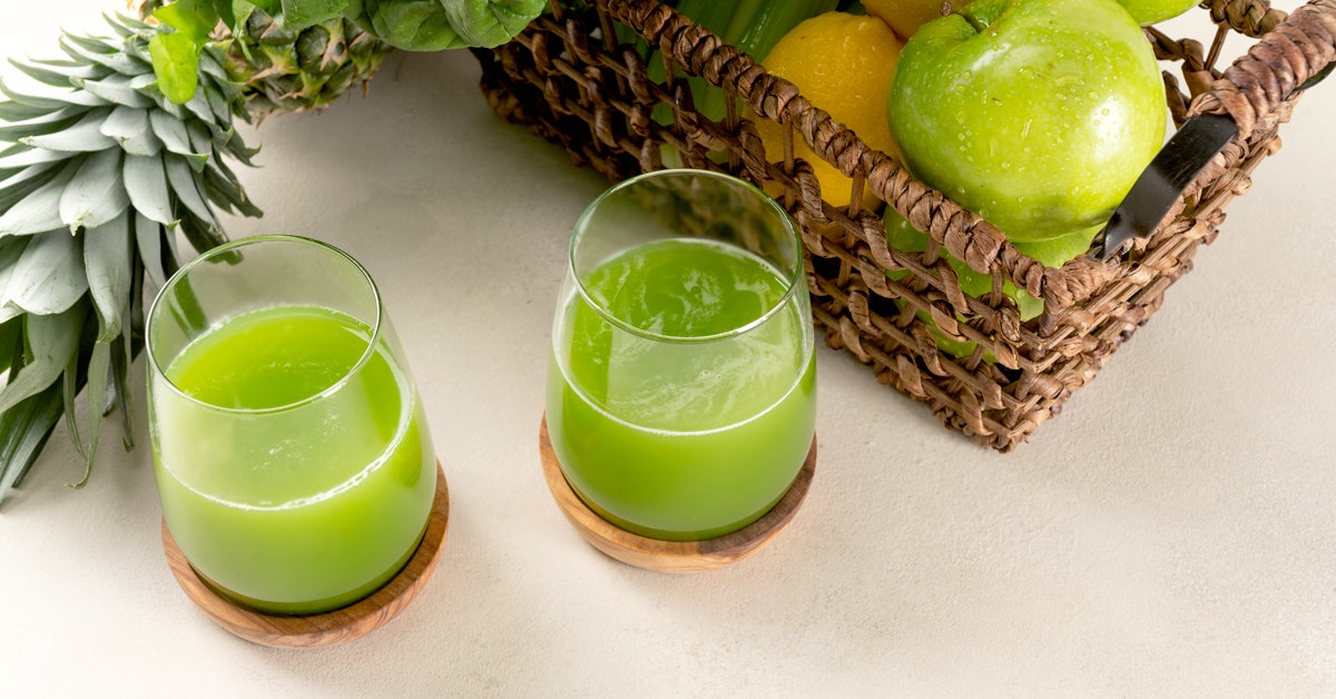 two glasses of anti inflammation green juice on a white table next to a basket of ingredients