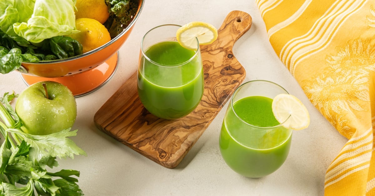 two glasses of green cabbage juice on a wooden cutting board