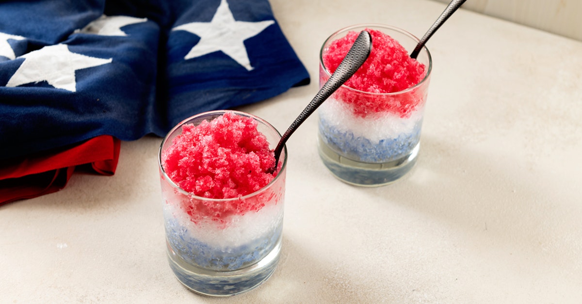 red white and blue granita in two glasses on a white table next to an American flag