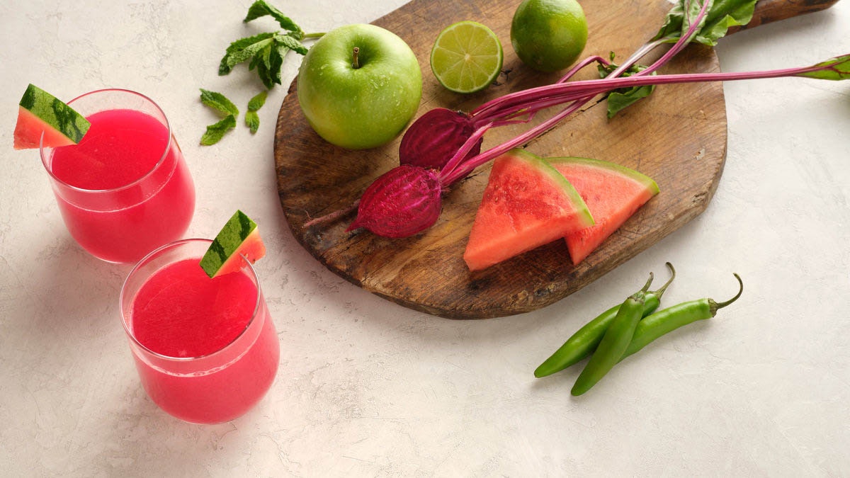 two glasses of cold pressed watermelon juice with green apple, lime, beet and chilies on a wooden cutting board
