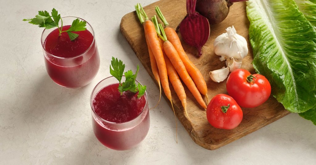 homemade V8 juice on a table with tomatoes and recipe ingredients