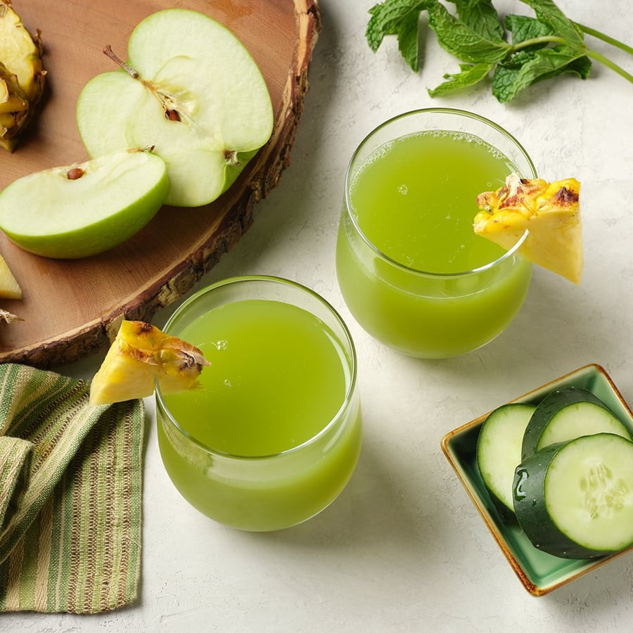 two glasses of cold pressed green juice made with mint, pineapple, green apple and cucumber on a white surface