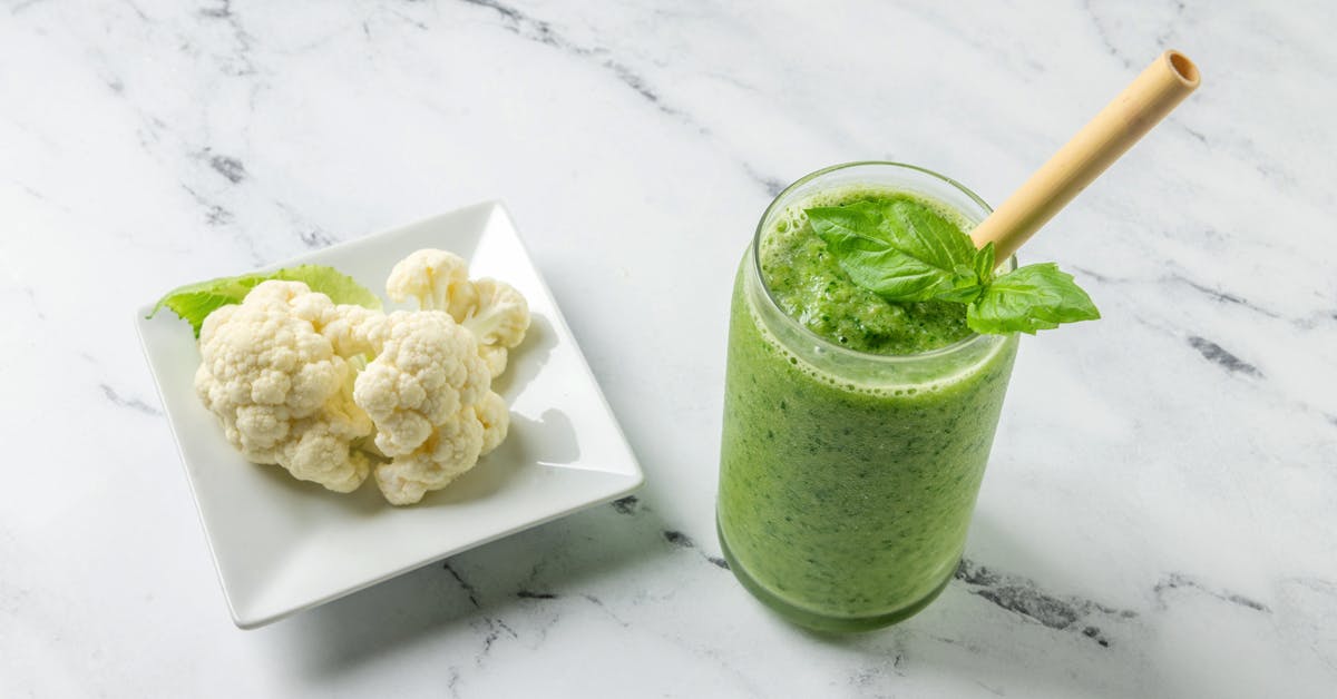 cauliflower green smoothie on a marble counter next to a plate of cauliflower