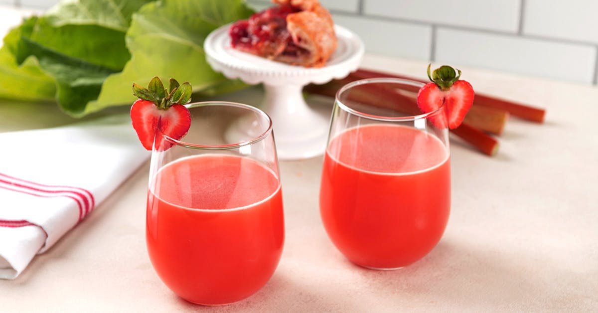 strawberry rhubarb juice next to pie on a white table