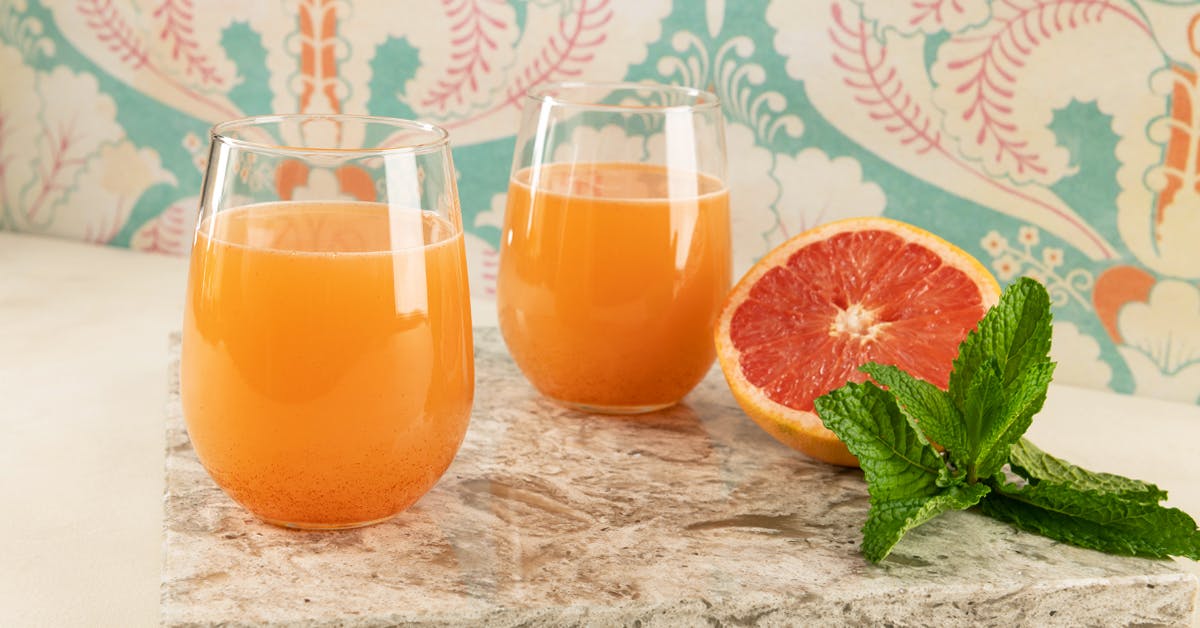 grapefruit juice recipe two glasses on a table with a half grapefruit and mint leaf