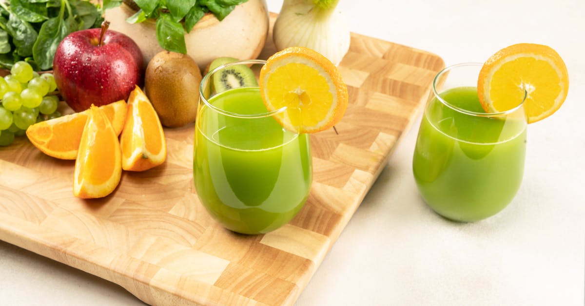 two glasses of green kiwi juice on a wooden cutting board