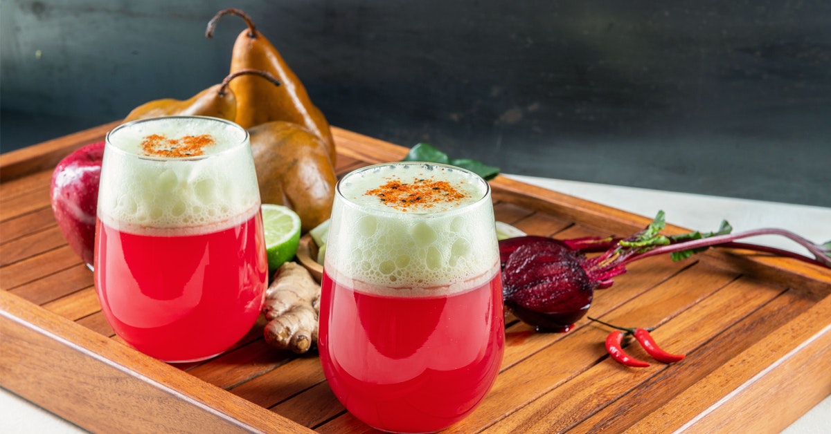 two glasses of spicy Thai cider on a wooden serving tray surrounded by recipe ingredients