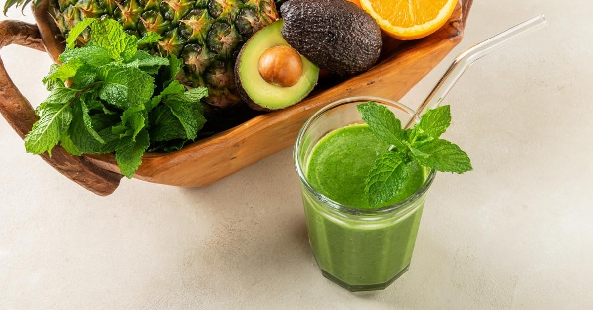glass of microgreen avocado smoothie on a table next to a basket of ingredients