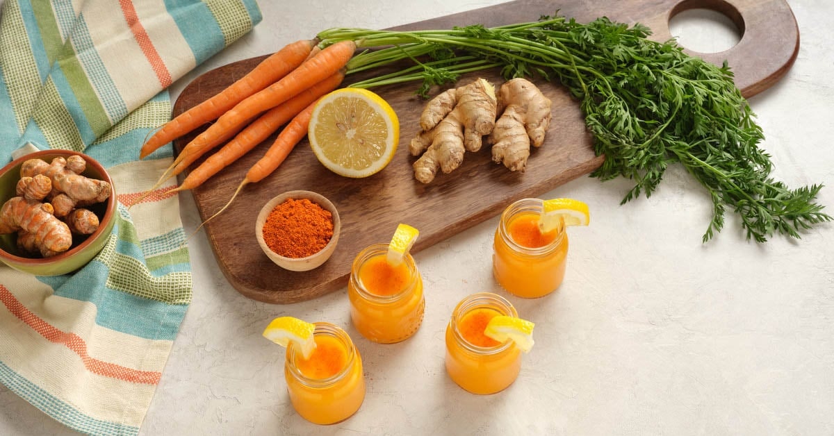 juice shots surrounded by the ingredients carrot, lemon, ginger, and turmeric to make this cold press wellness shot recipe