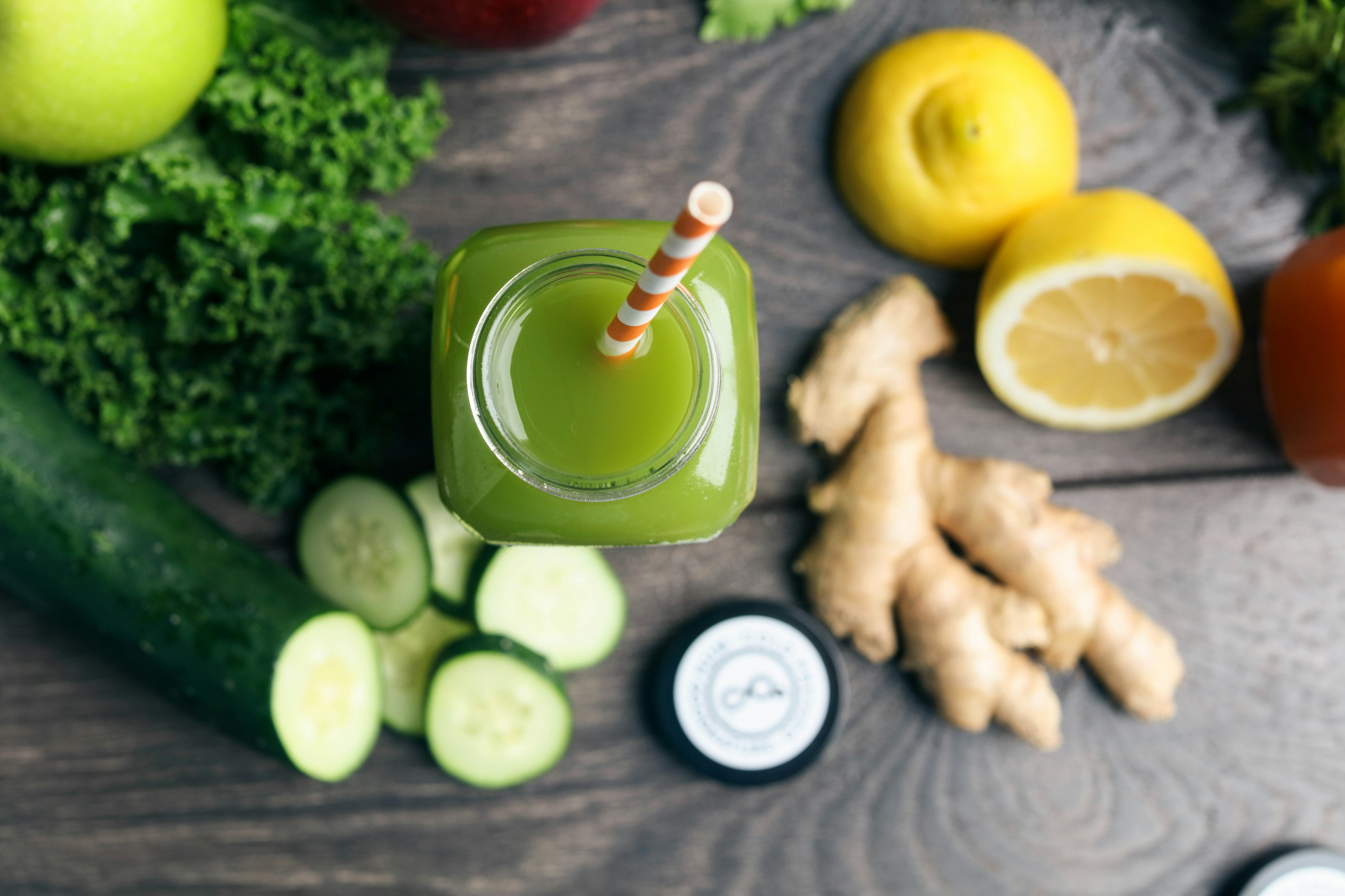 overhead shot of a bottle of green juice with a straw next to juicing ingredients