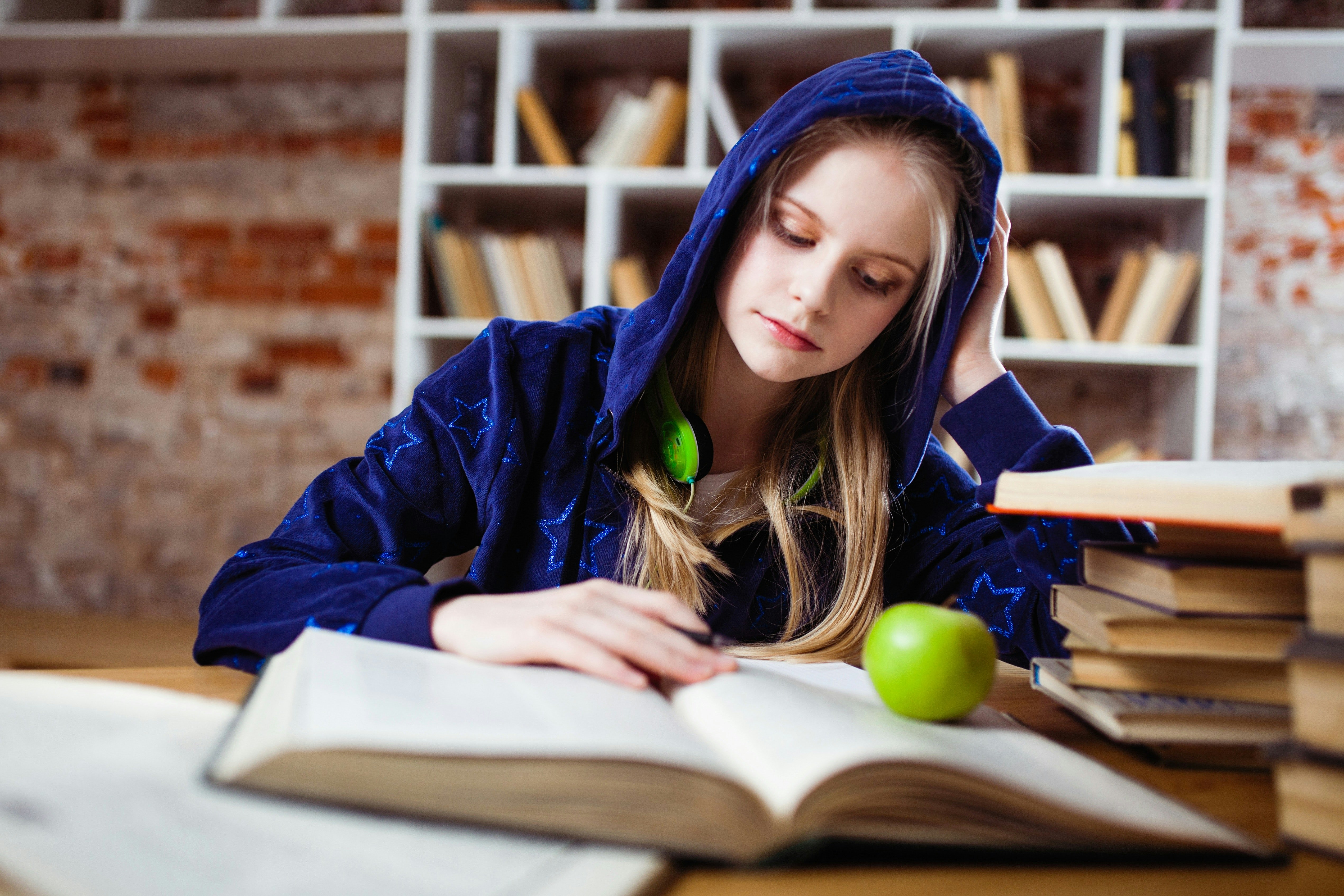 A tired girl studying with an apple wondering if there's caffeine in apple juice.