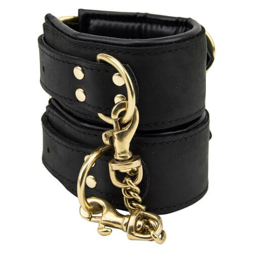 Black leather wrist cuffs with gold rings and a clip on the chain