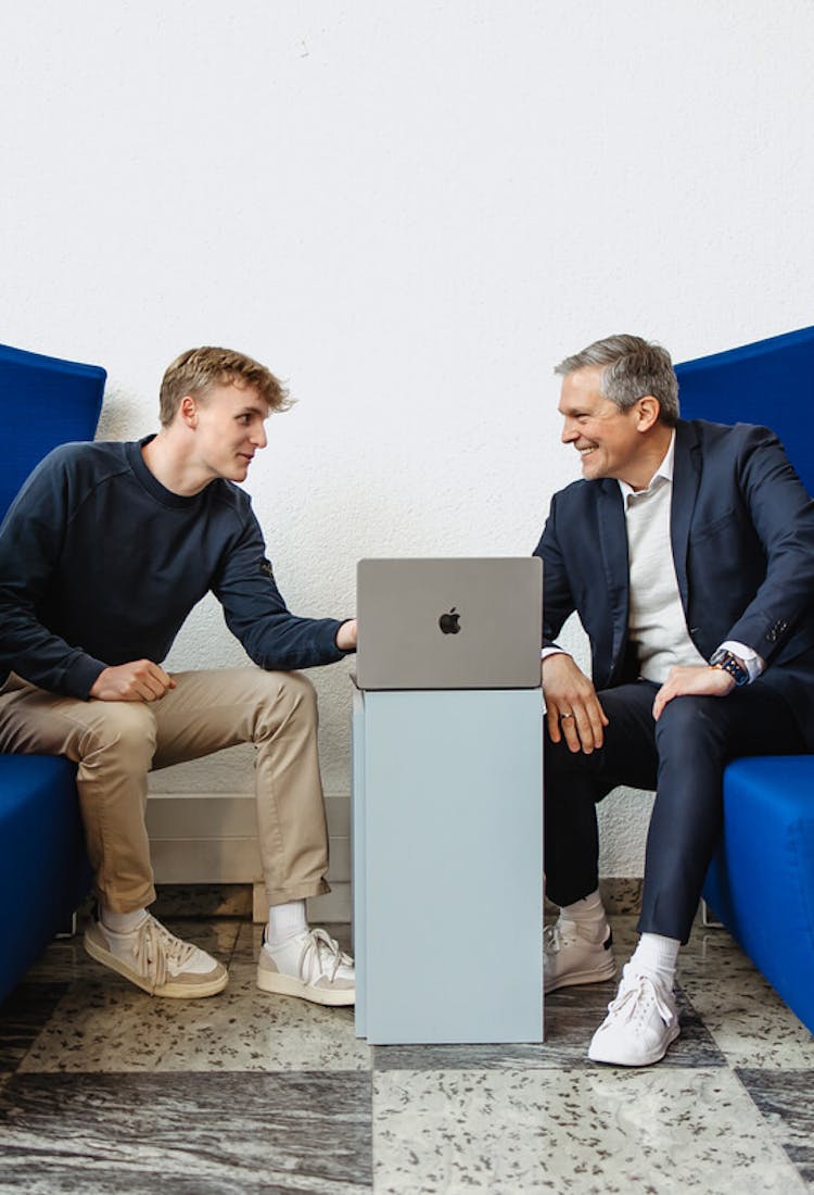 Zwei Männer beugen sich über MacBook und diskutieren