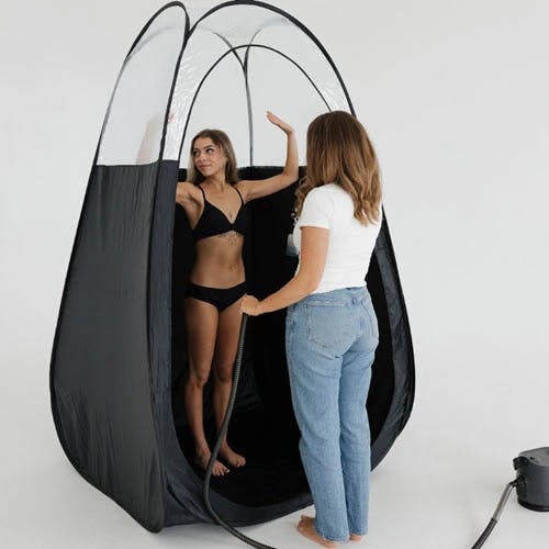 Grace training a student with a spray-tanning demonstration.