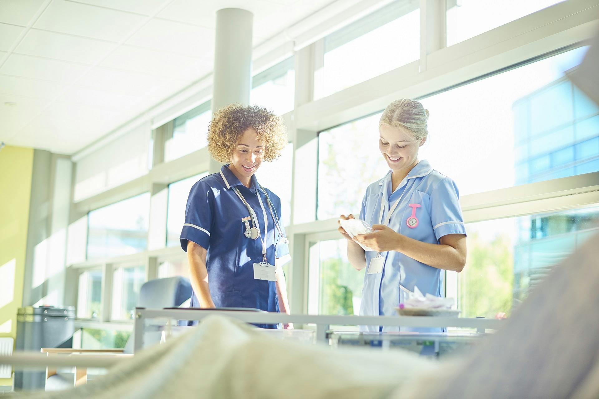 Two nurses in discussion while standing beside a patient.