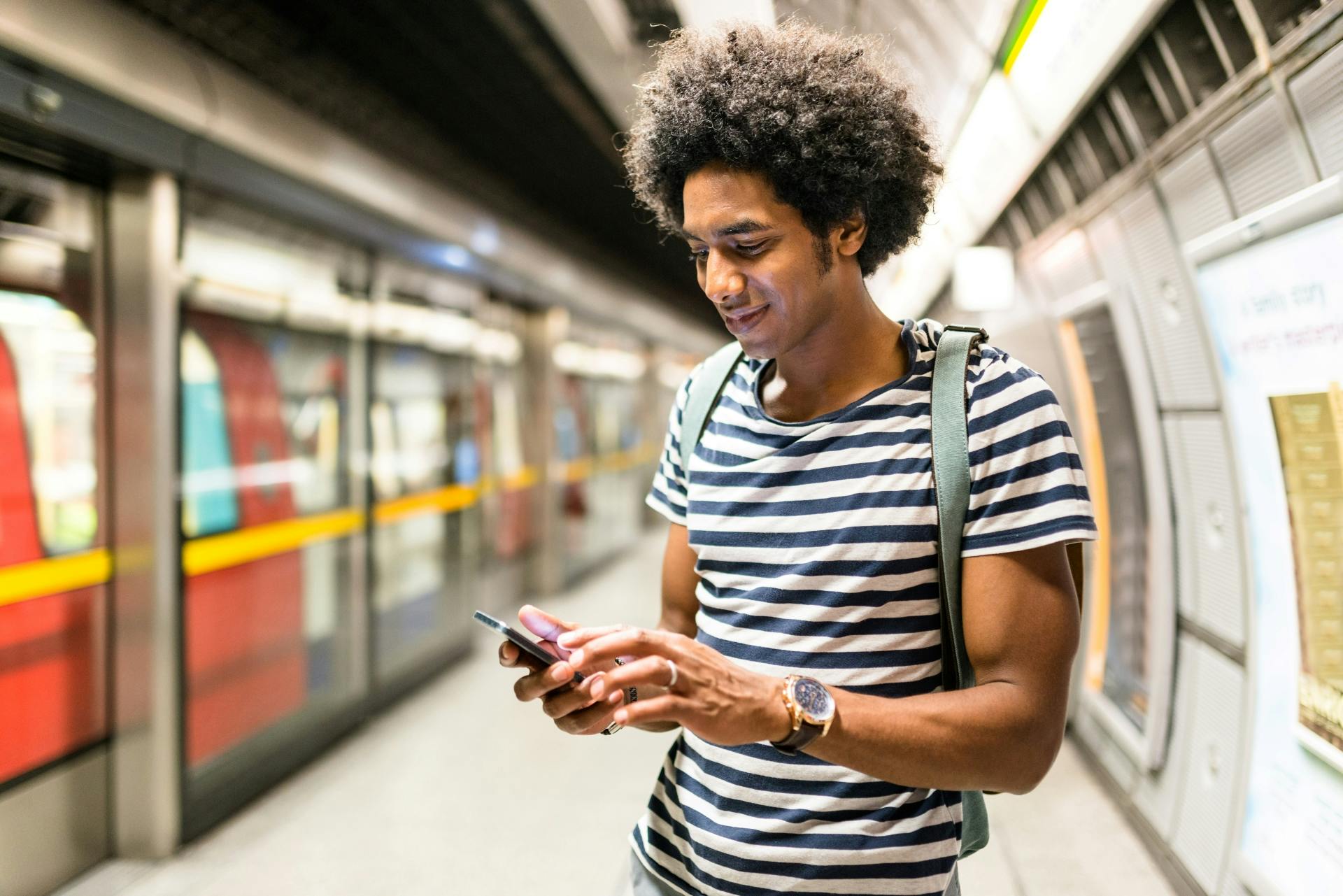 A young person checks their phone while standing on a London Underground platform.