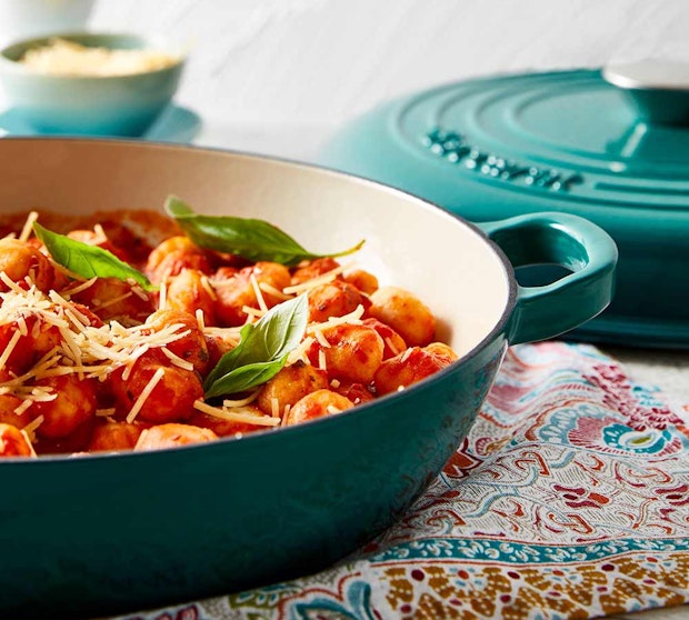Baccarat Le Connoisseur Dutch Ovens, Saute pans and Baking Dishes. Saute pan with pasta dish resting on a multi coloured tea towel.