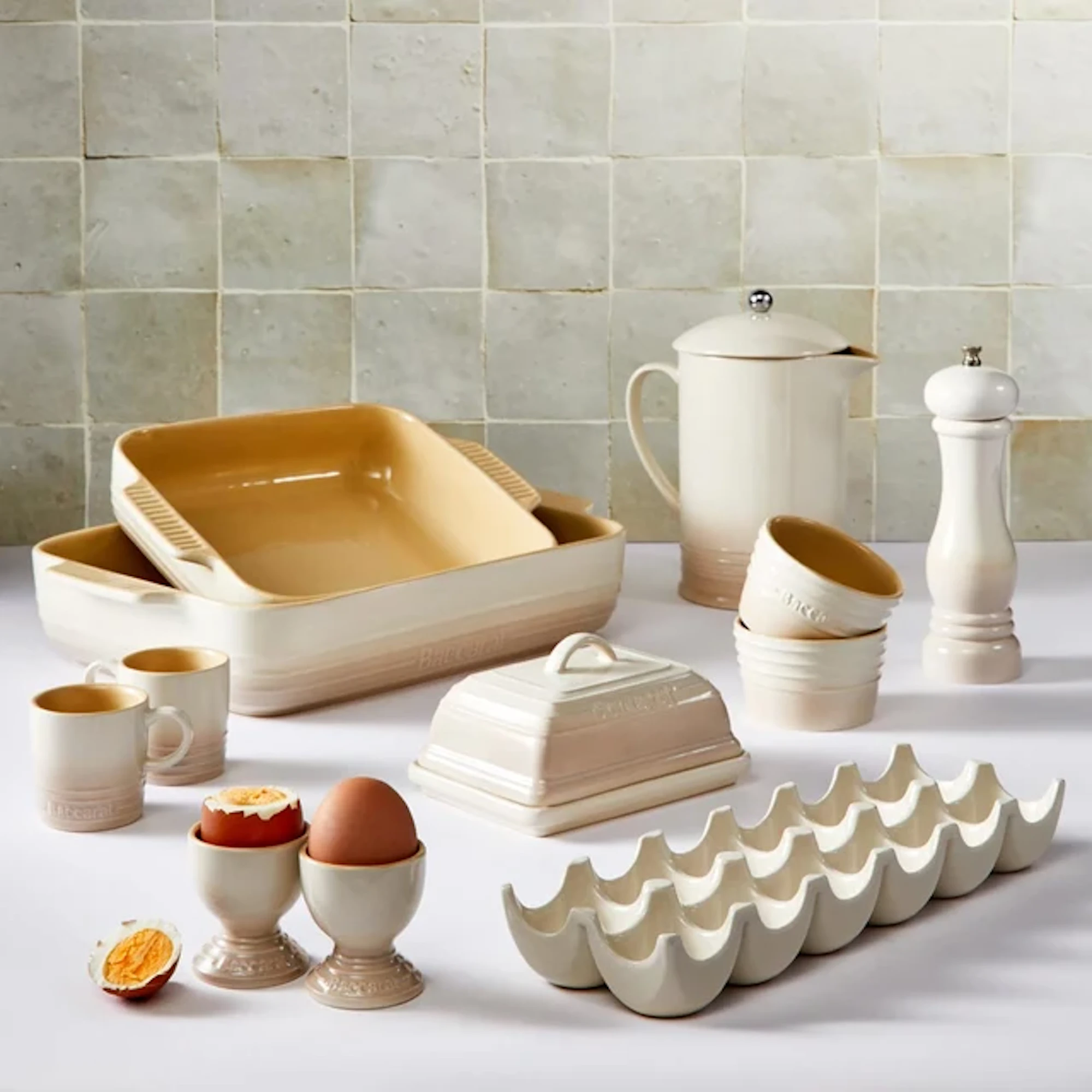 Cream-colored kitchenware is arranged on a surface against a tiled wall.