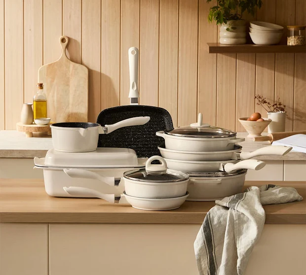 White cookware sets are stacked on a kitchen counter in front of a wooden panel wall.