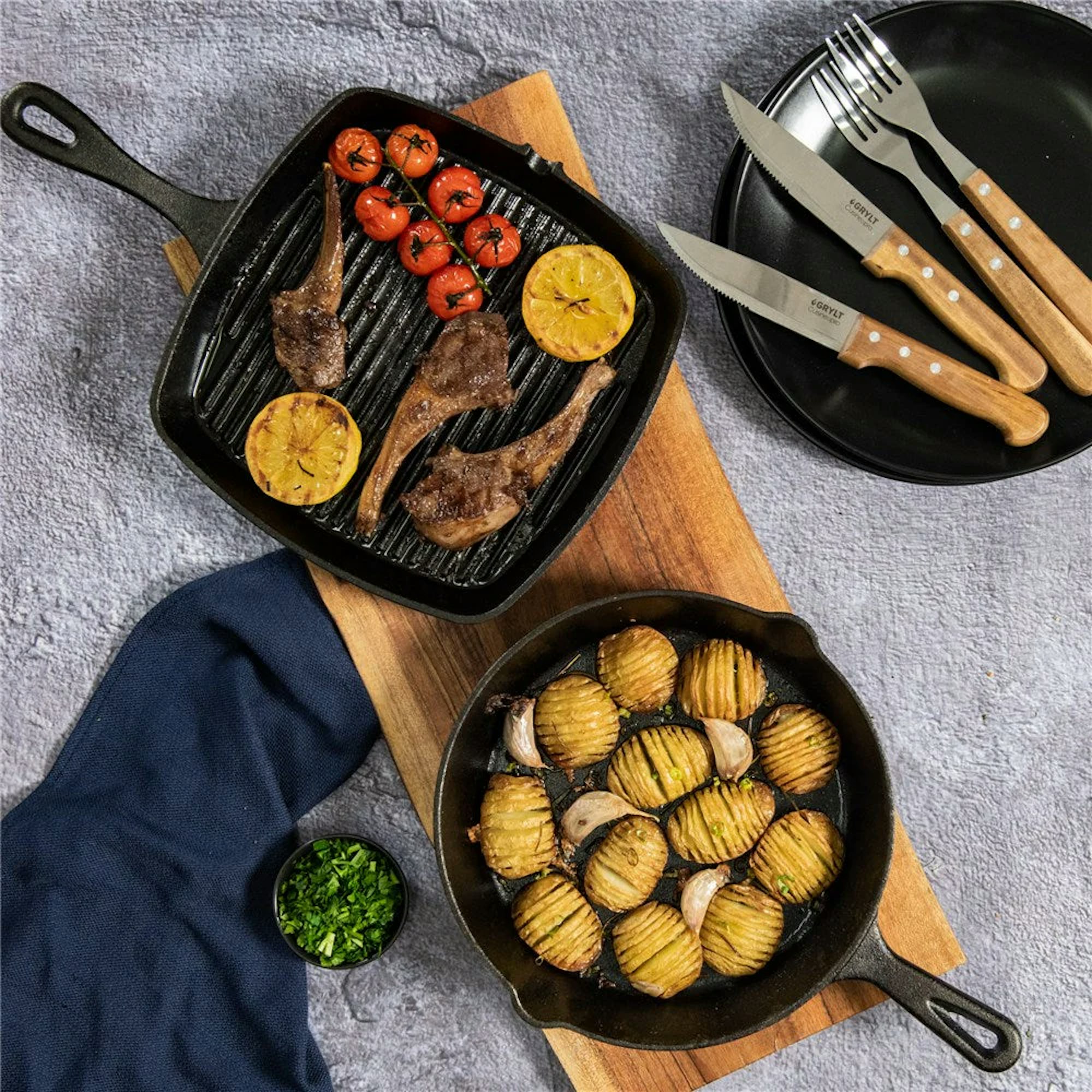 Two black cast iron pans, one square and one round with grilled food cooking in them