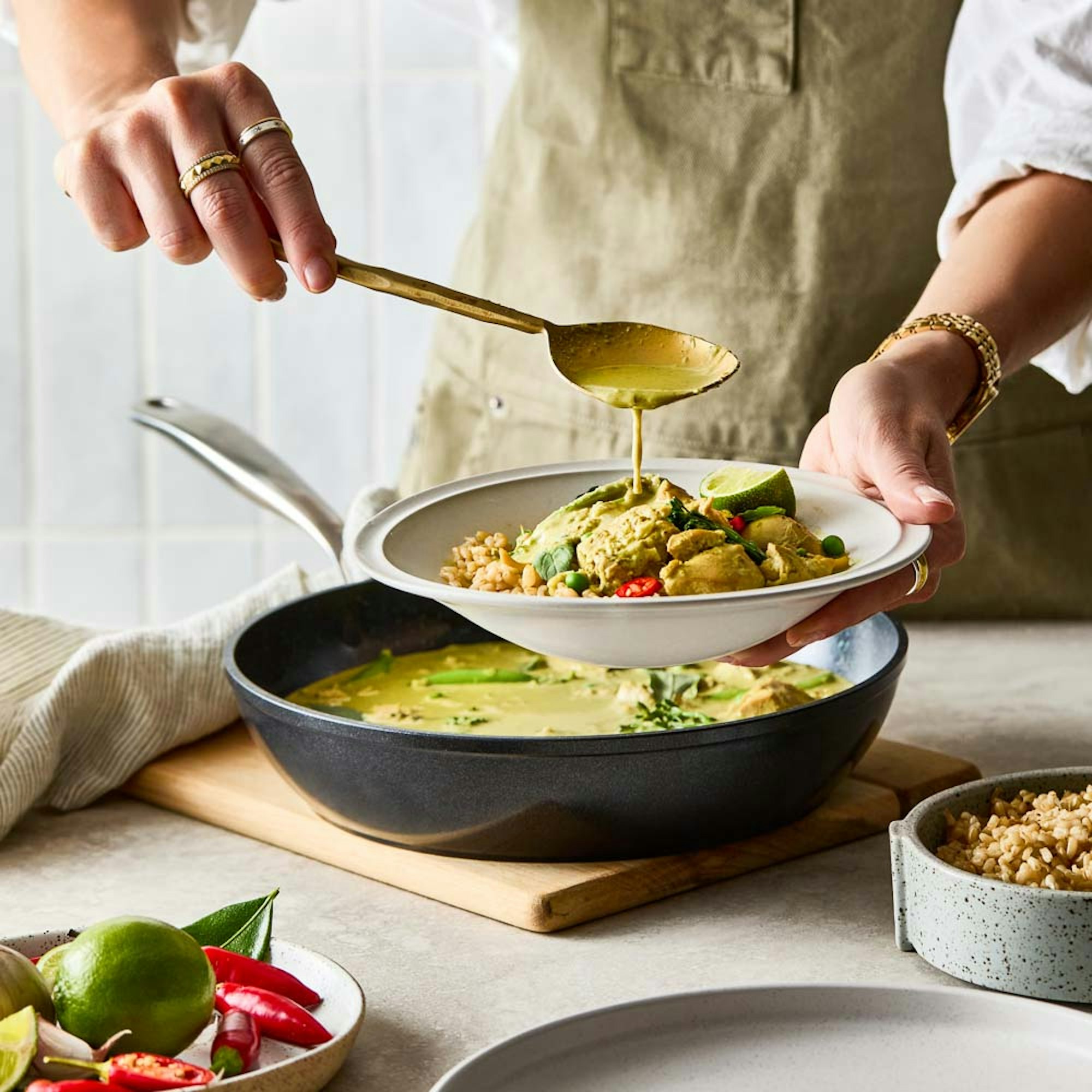 Woman serving thai green chicken curry from frypan to a bowl. Baccarat GREEN STONE® 28cm frypan.