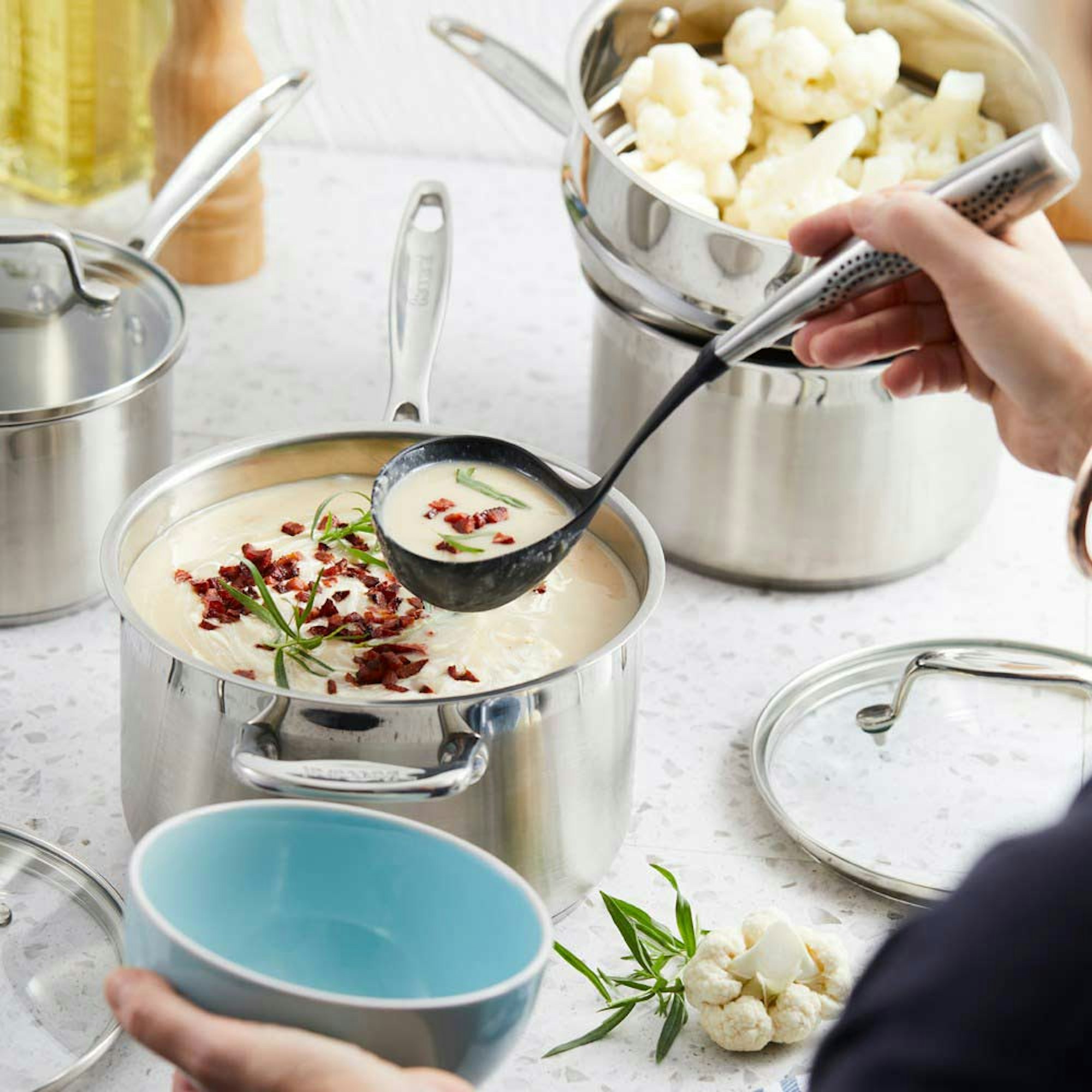 Top Reasons to Invest Quality Cookware blog. Woman serving cauliflower soup from stainless steel cookware.