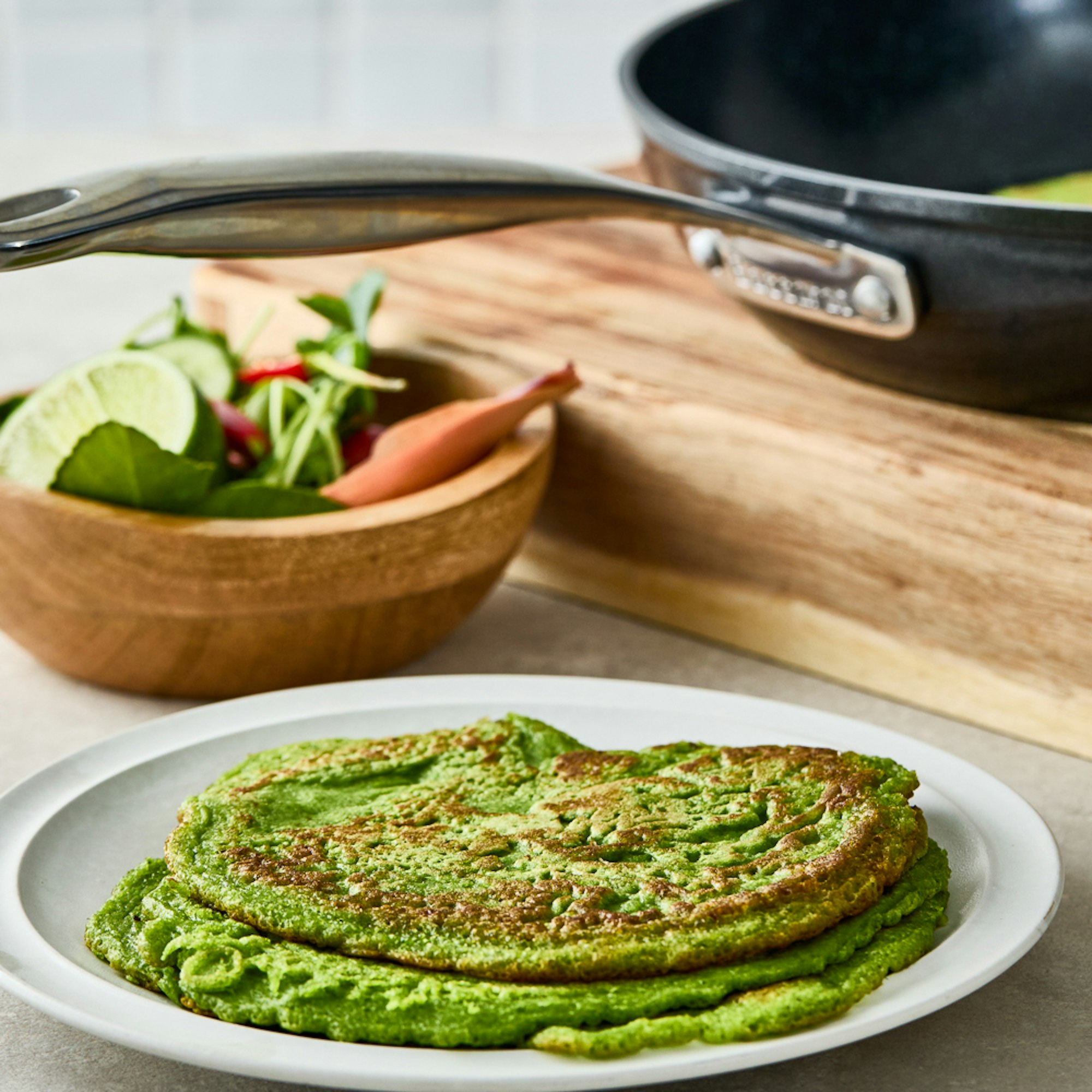 Stack of super greens pancakes with a side salad next to a frypan. Baccarat Super Greens Pancakes recipe