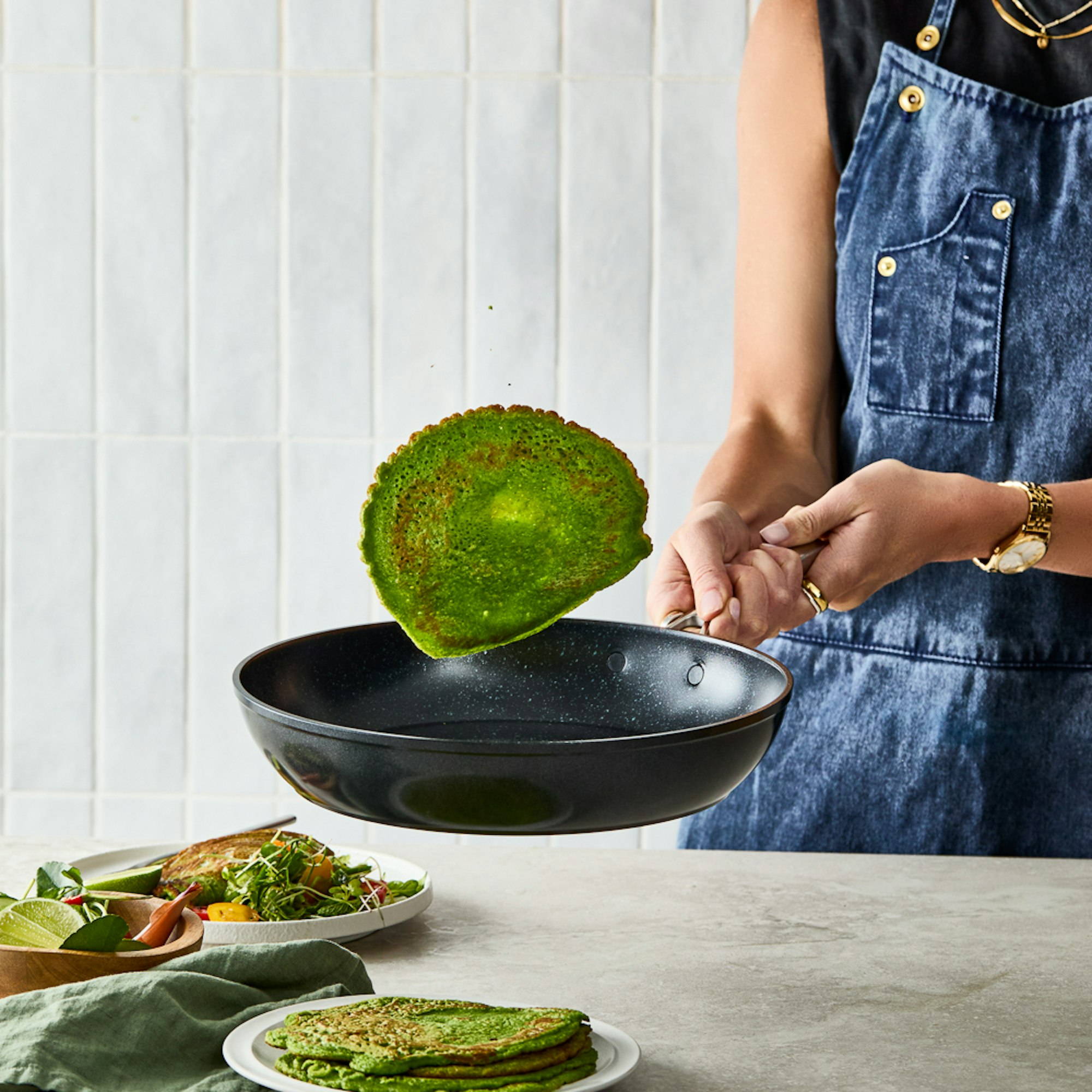 Woman flipping green pancake next to stack of green pancakes. Super Greens pancakes recipe.