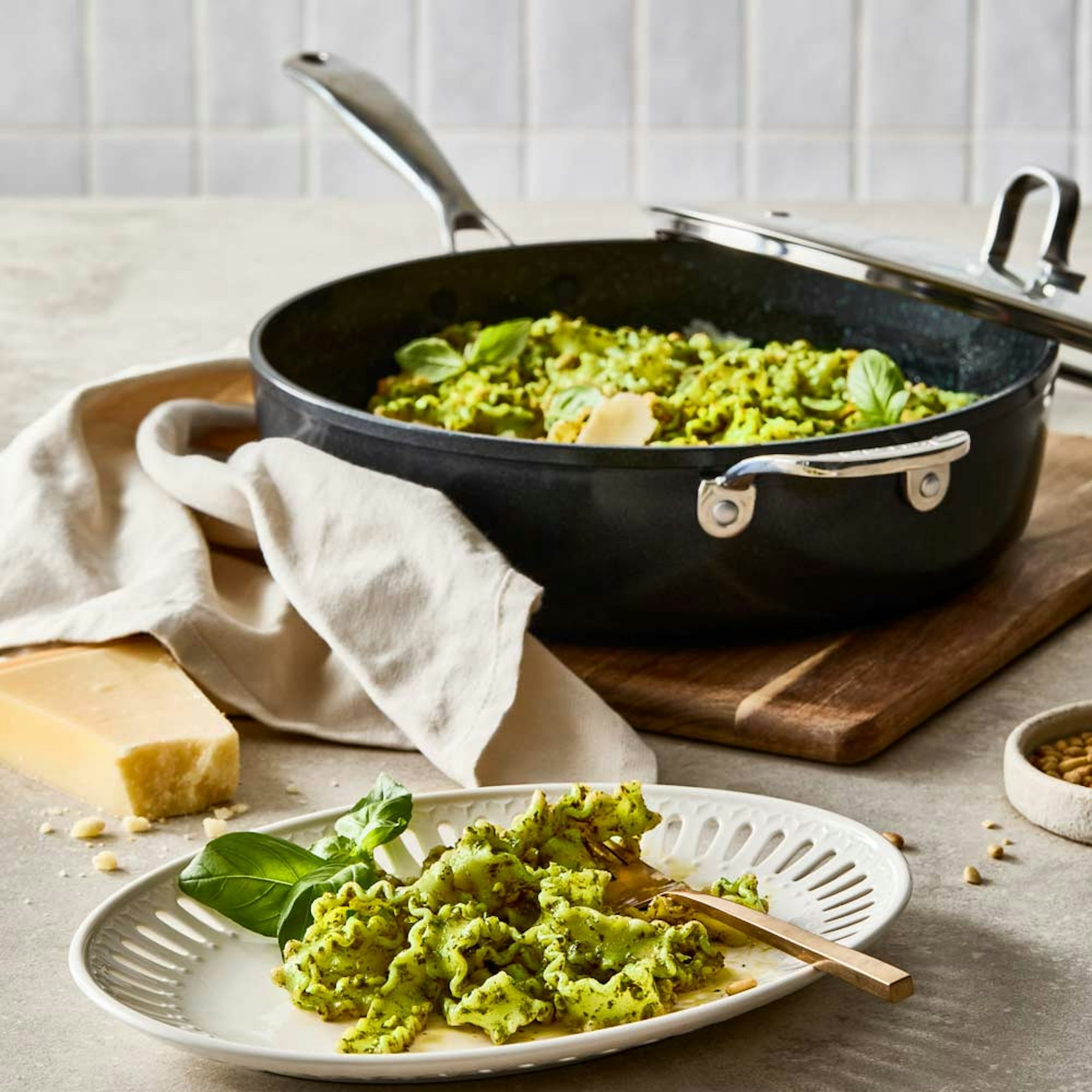 A plate of pesto pasta on the side with frypan with lid in the background. Baccarat GREEN STONE Chef pan.