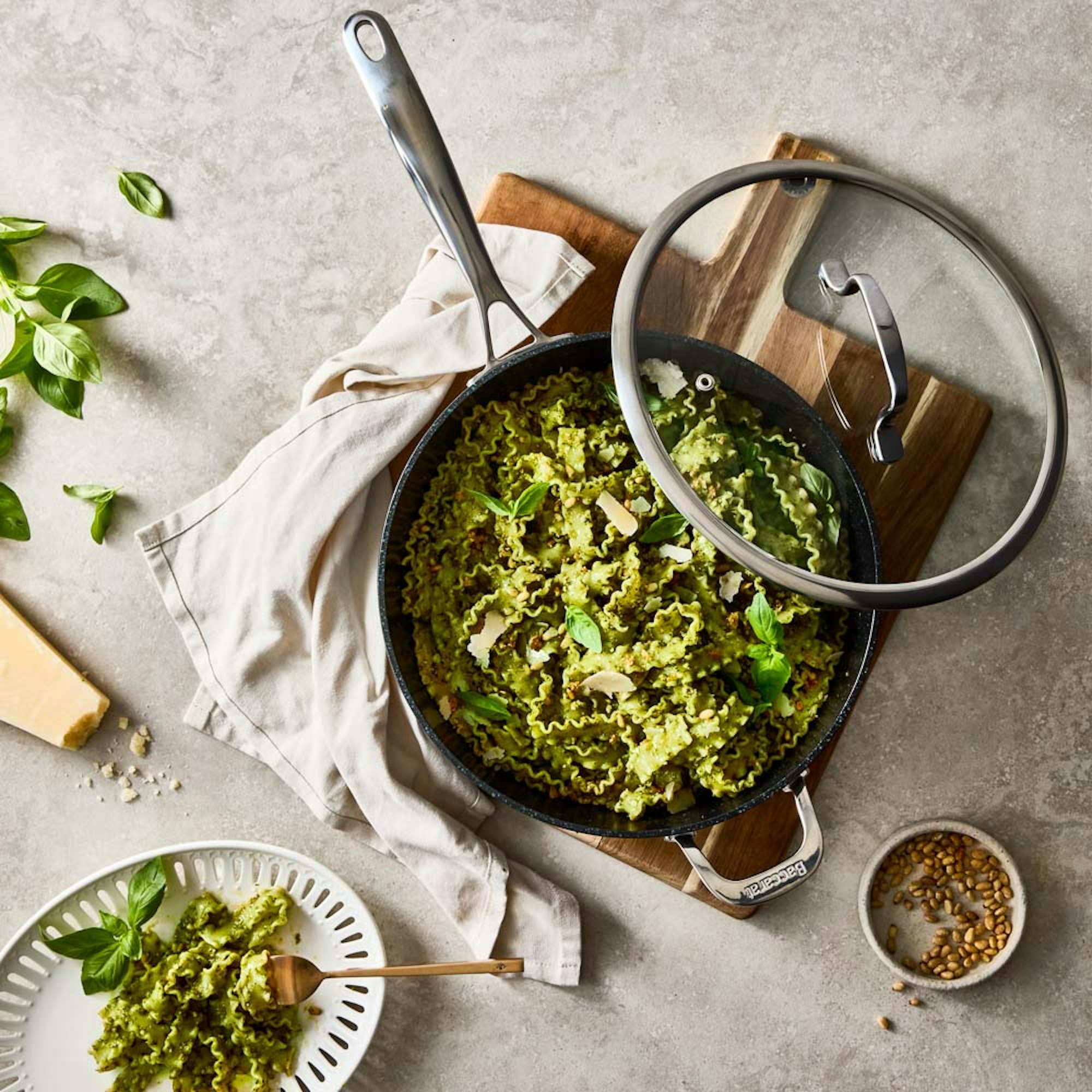 Flat lay shot of pesto pasta in frypan with lid a plate of pasta on the side. Baccarat GREEN STONE Chef pan.