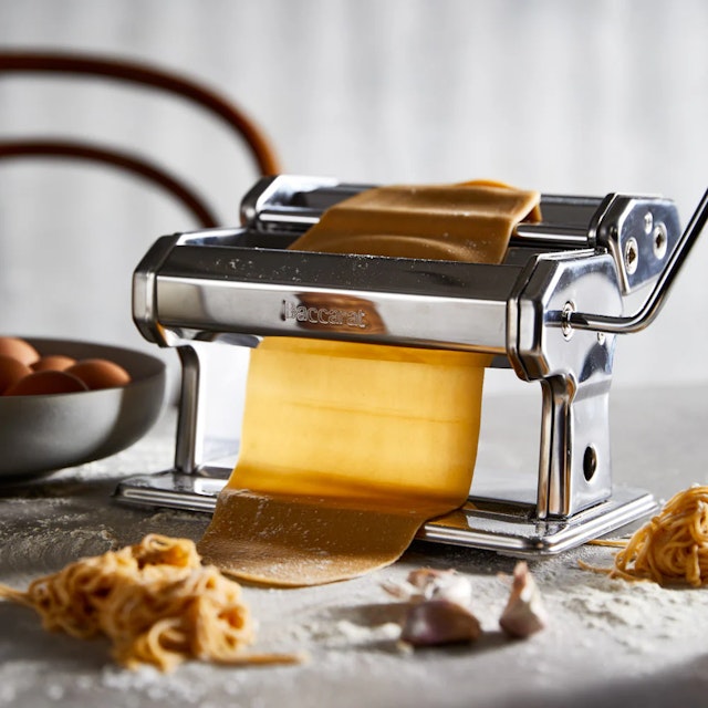 Silver pasta maker on a bench with a roll of pasta going through it