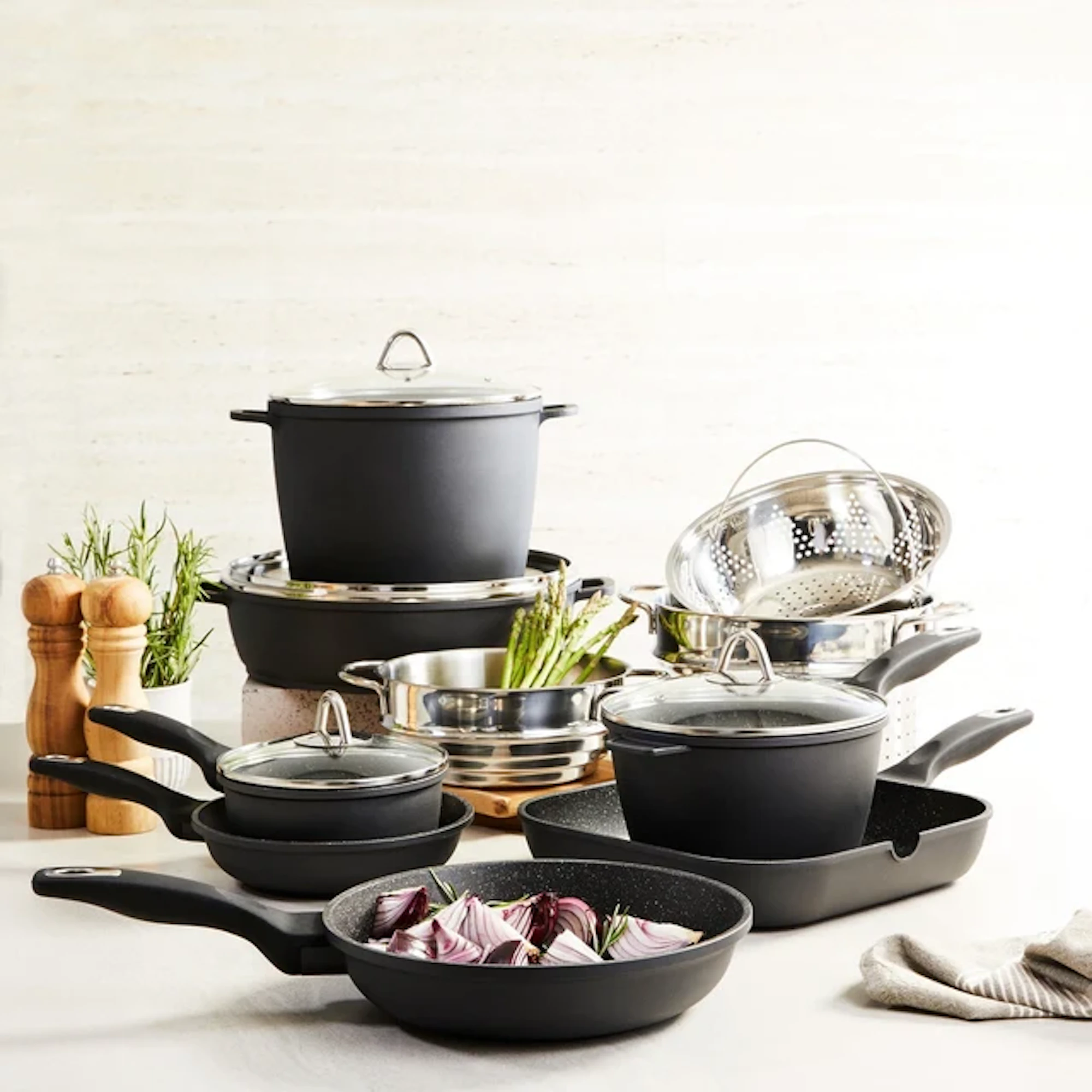 A collection of various black granite cookware pieces is arranged on a light-colored surface.