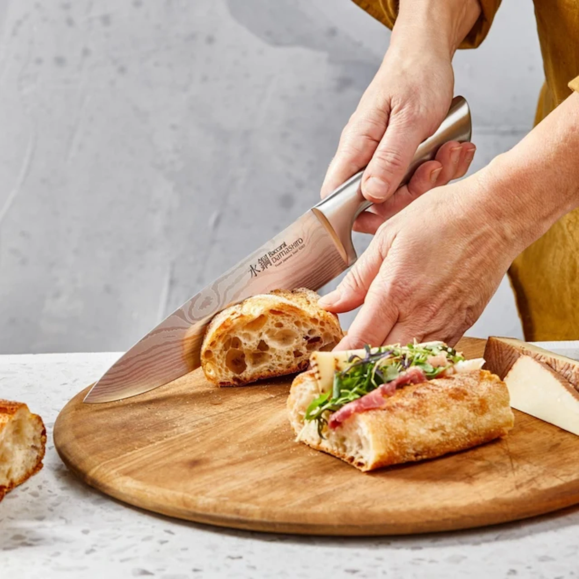 A person is slicing bread on a wooden board with a knife.