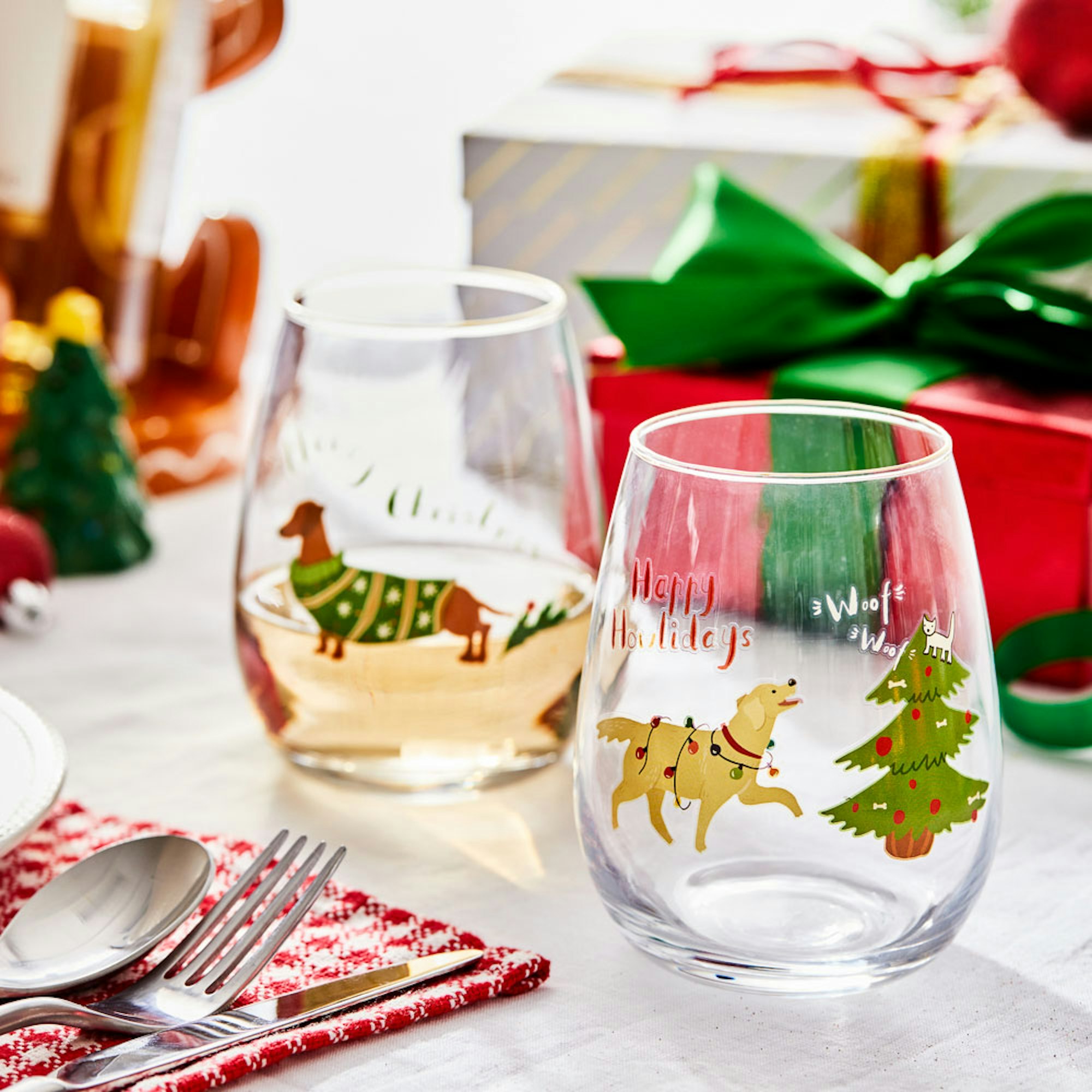 Christmas Gift Guide. Secret Santa Gifts. Two Christmas stemless wine glasses with presents in the background.