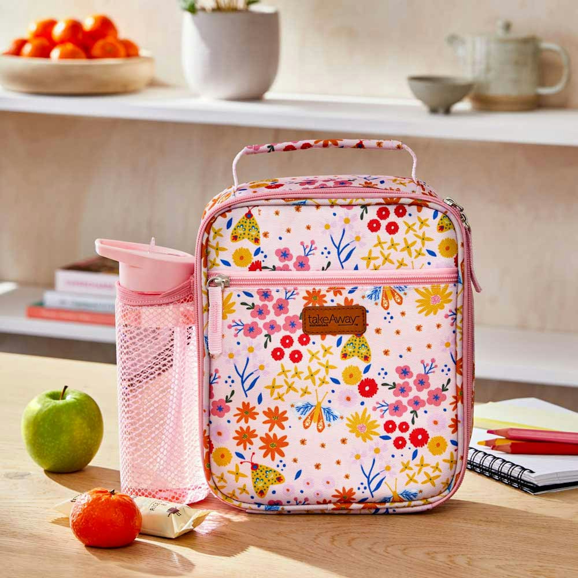 Takeaway Out Lunch bag set. Your Guide to Back to School preparation. Pink and floral lunch bag with drink bottle on the kitchen counter with fruit and books.