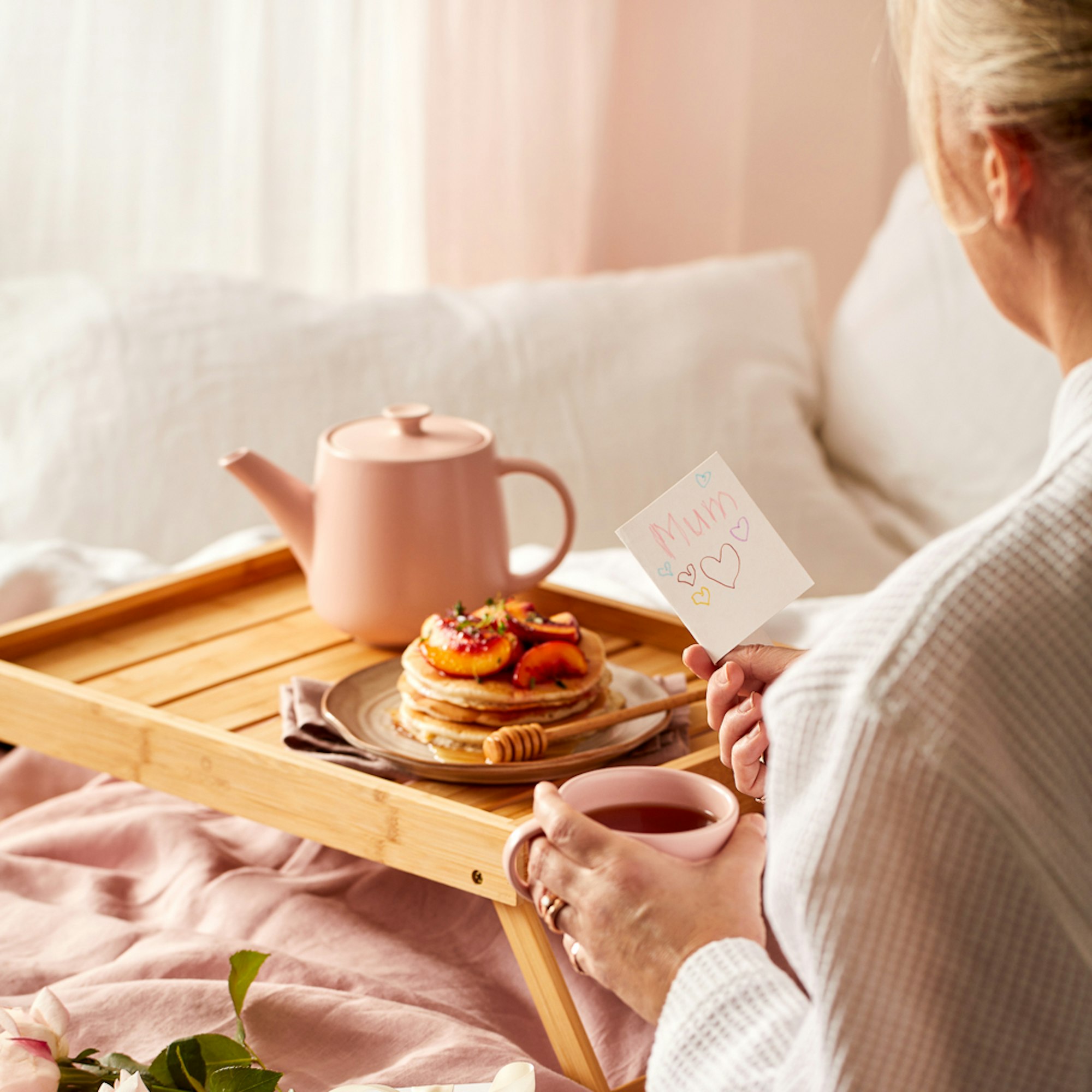 Mother’s Day Gift Guide 2023. Woman sitting in bed with breakfast reading Mother's Day card