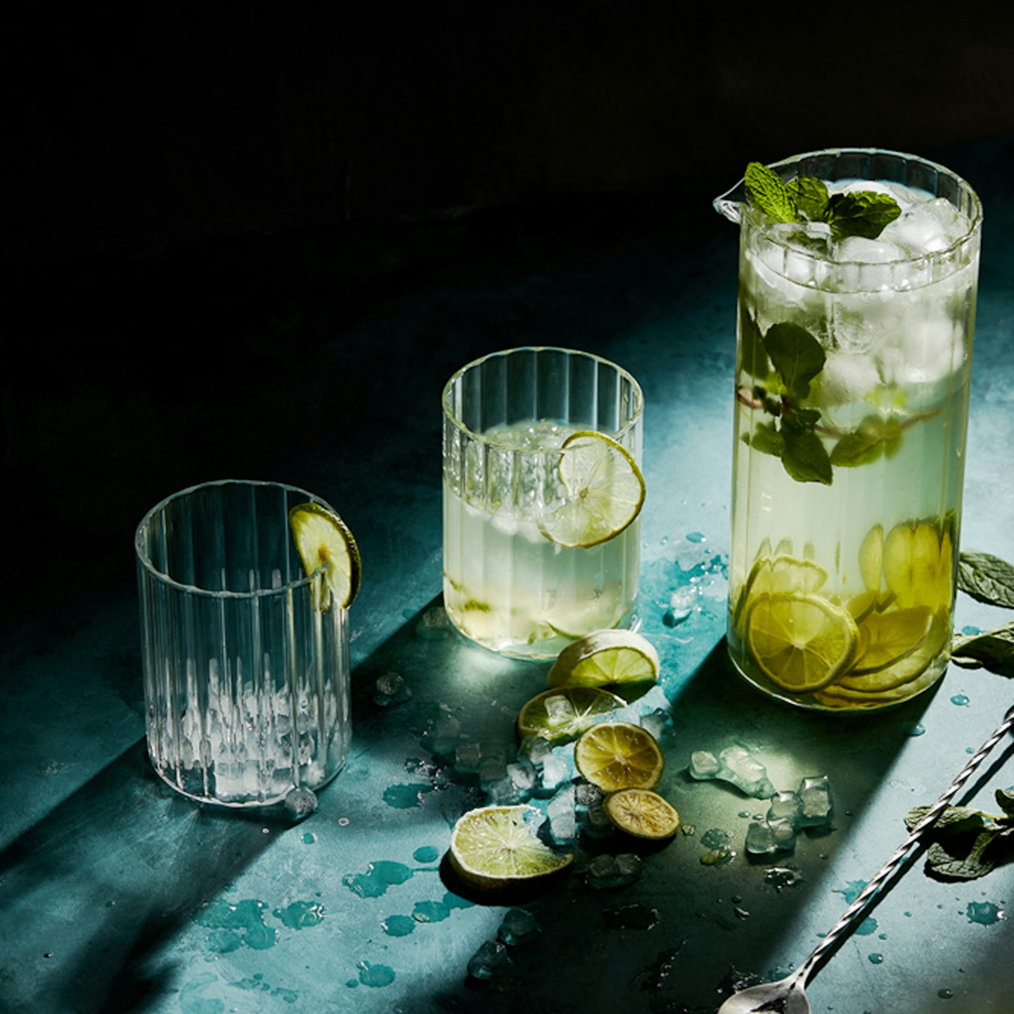 Ribbed jug filled with mojito cocktail and matching ribbed tumblers and cocktail stirrer