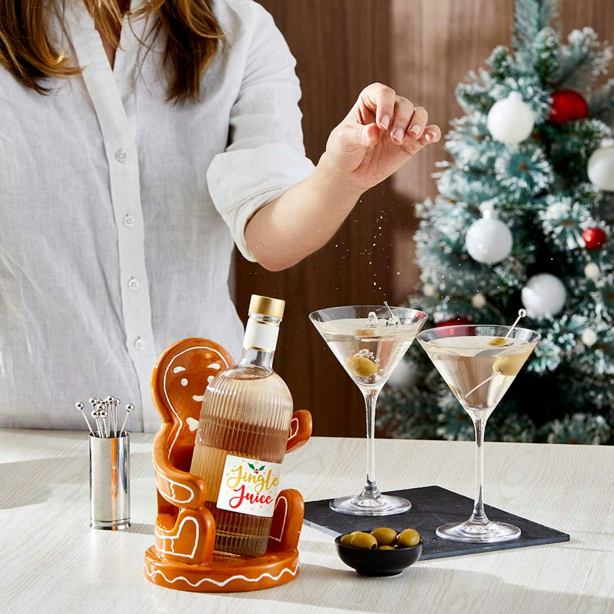 Christmas Gift Guide 2023. Gifts for colleagues. Gingerbread man bottle holder with woman sprinkling salt into a martini glass.