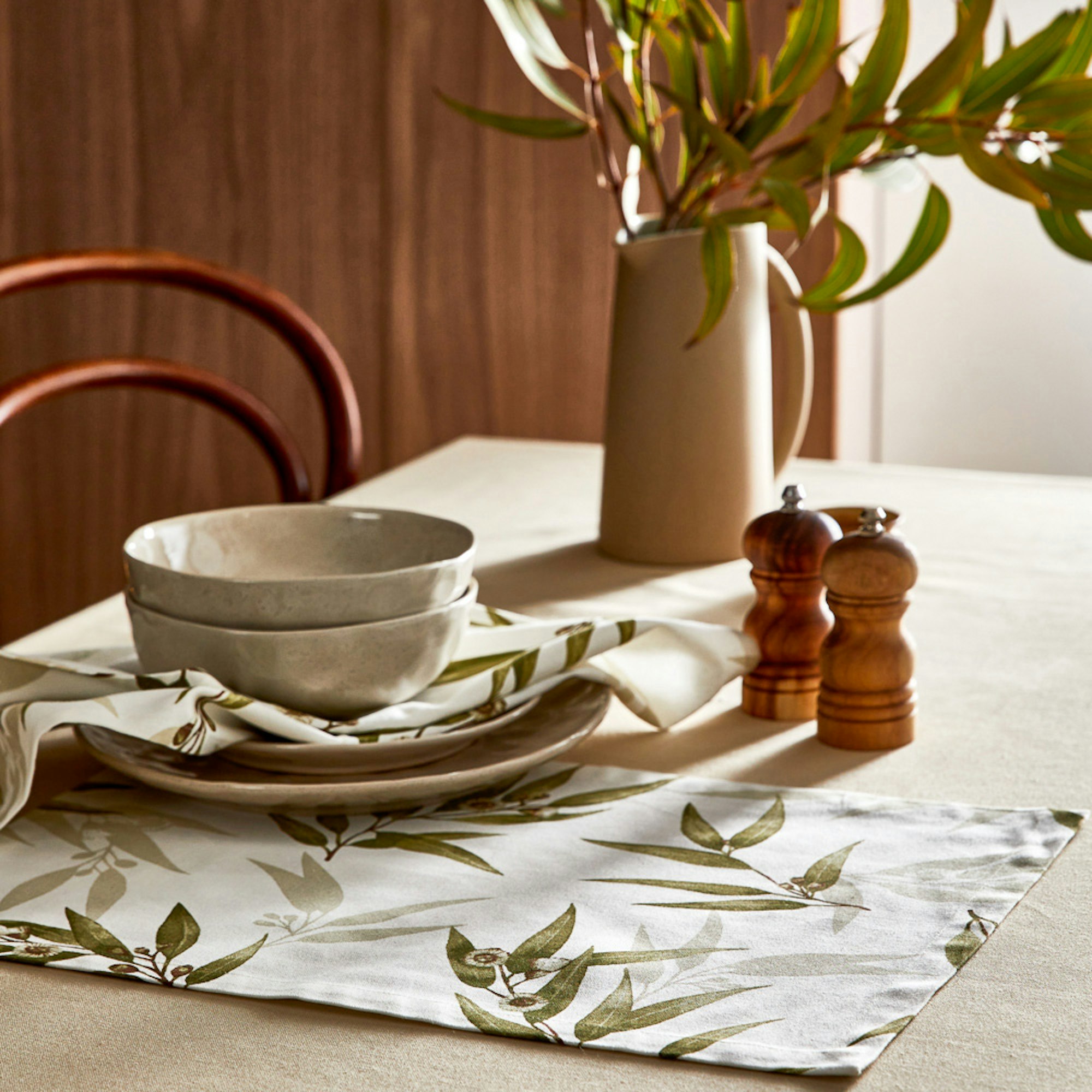 MyHouse SS23 collection. Gum leaf placemats on table setting with bowls and plates stacked and a jug of natives.