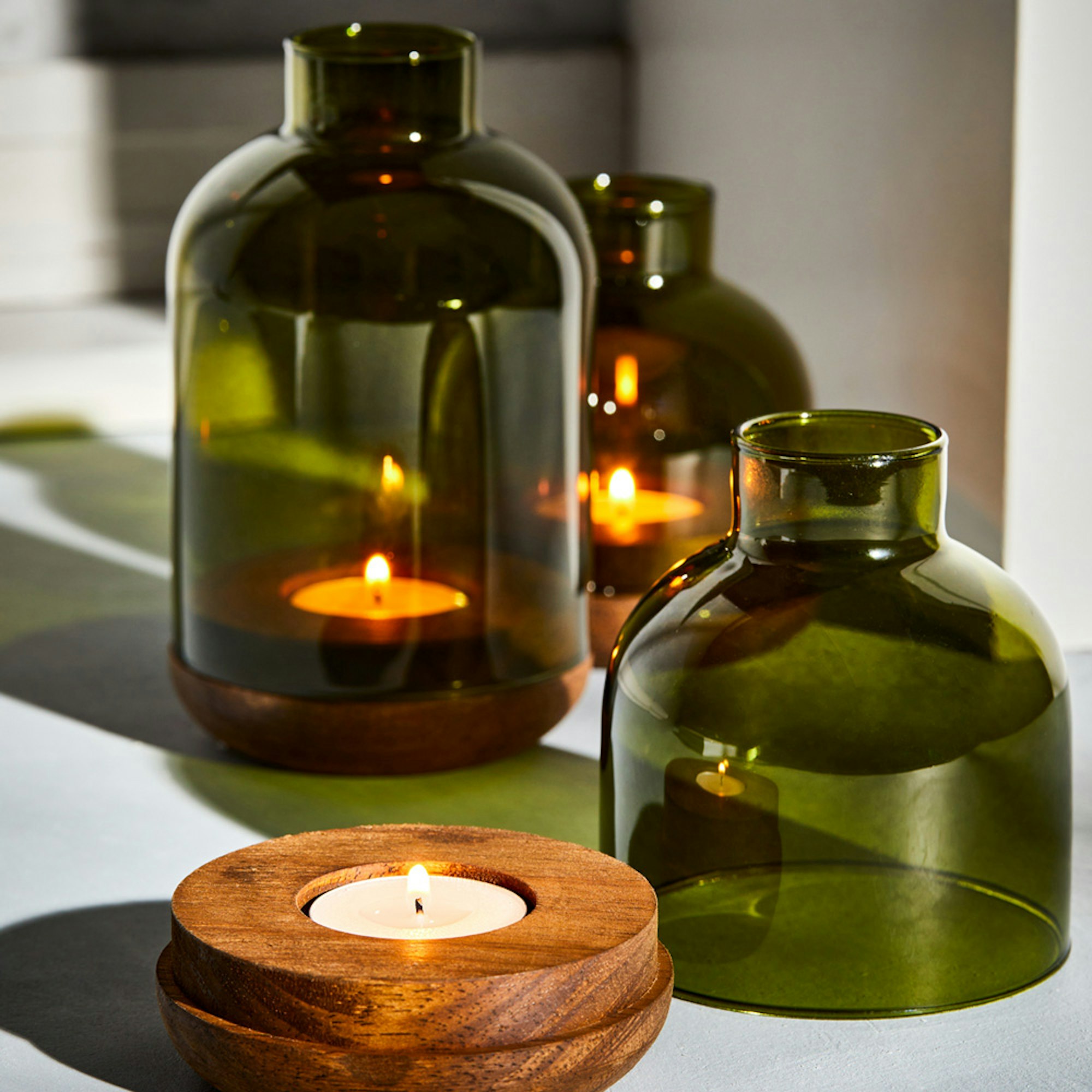 Neale Whitaker SS23 Cloche in Green. Set of 3 green cloches with wooden bases lit with tealight candles.