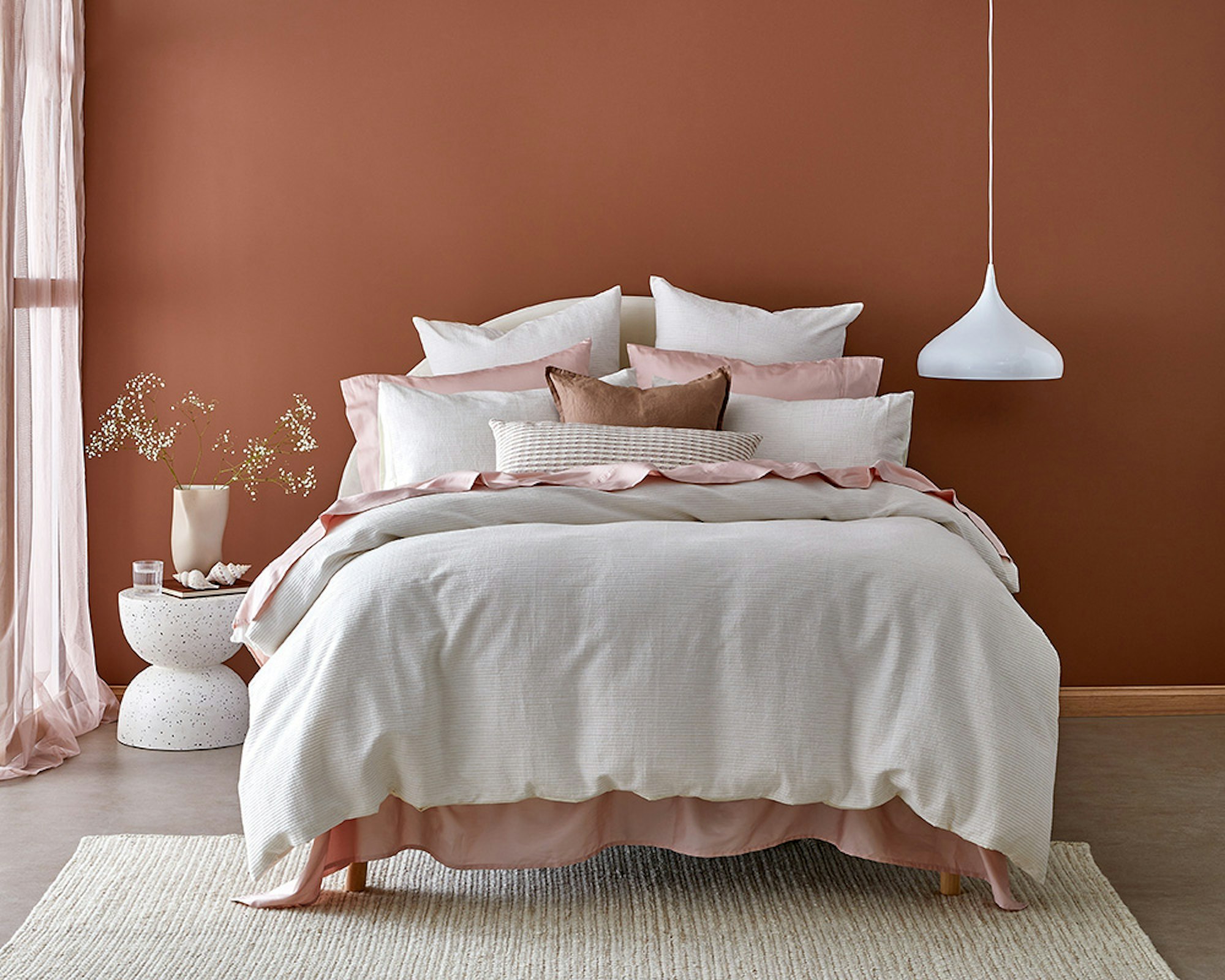 Home Beautiful Collection. Haven Quilt Cover Set. White quilt on bed with pink sheets and rust coloured walls. 