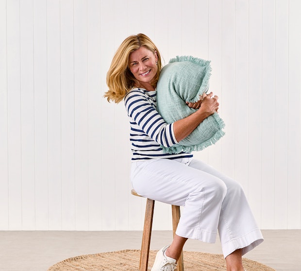Home with Deborah Hutton SS23 Collection. Deborah Hutton sitting on a stool hugging a cushion.