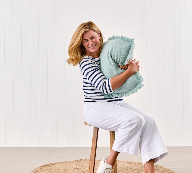 Home with Deborah Hutton SS23 Collection. Deborah Hutton sitting on a stool hugging a cushion.