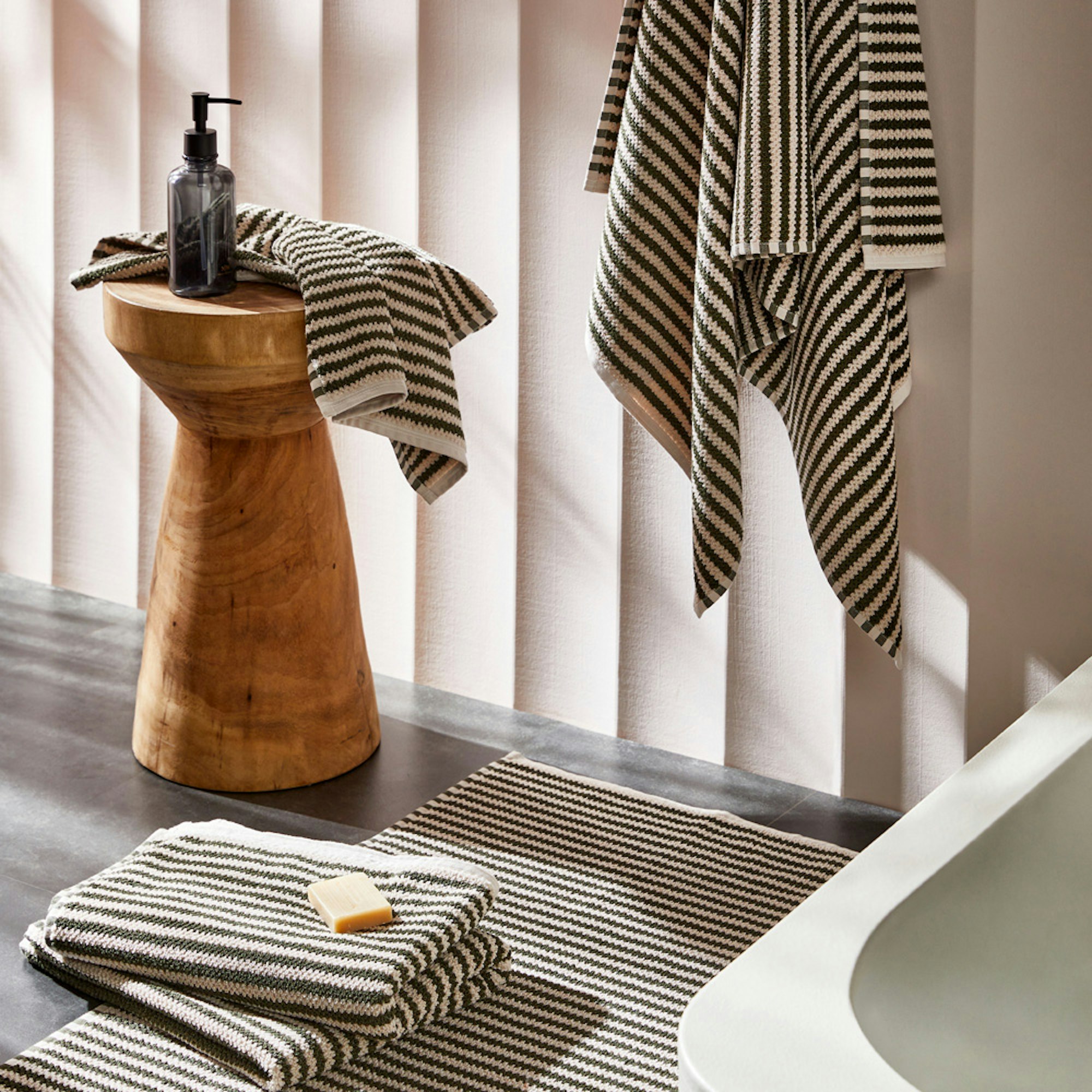 Neale Whitaker SS23 Turkish textured towel collection. Towel collection in green and white stripe in a bathroom setting.