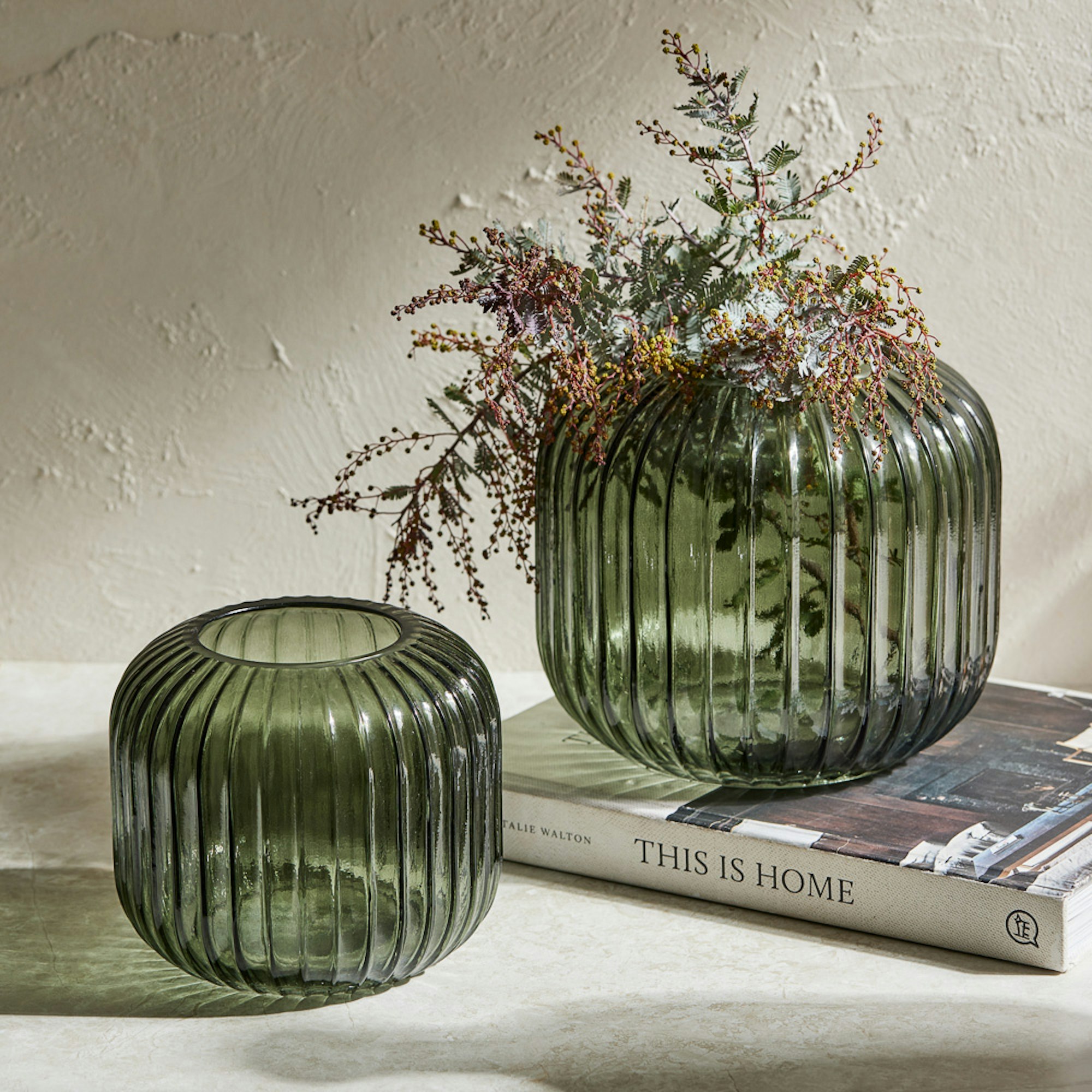 Two green ribbed vases with flowers sitting on books